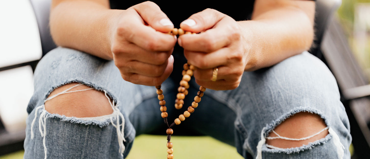 boy with rip knee blue jeans praying the rosary on wooden beads, 